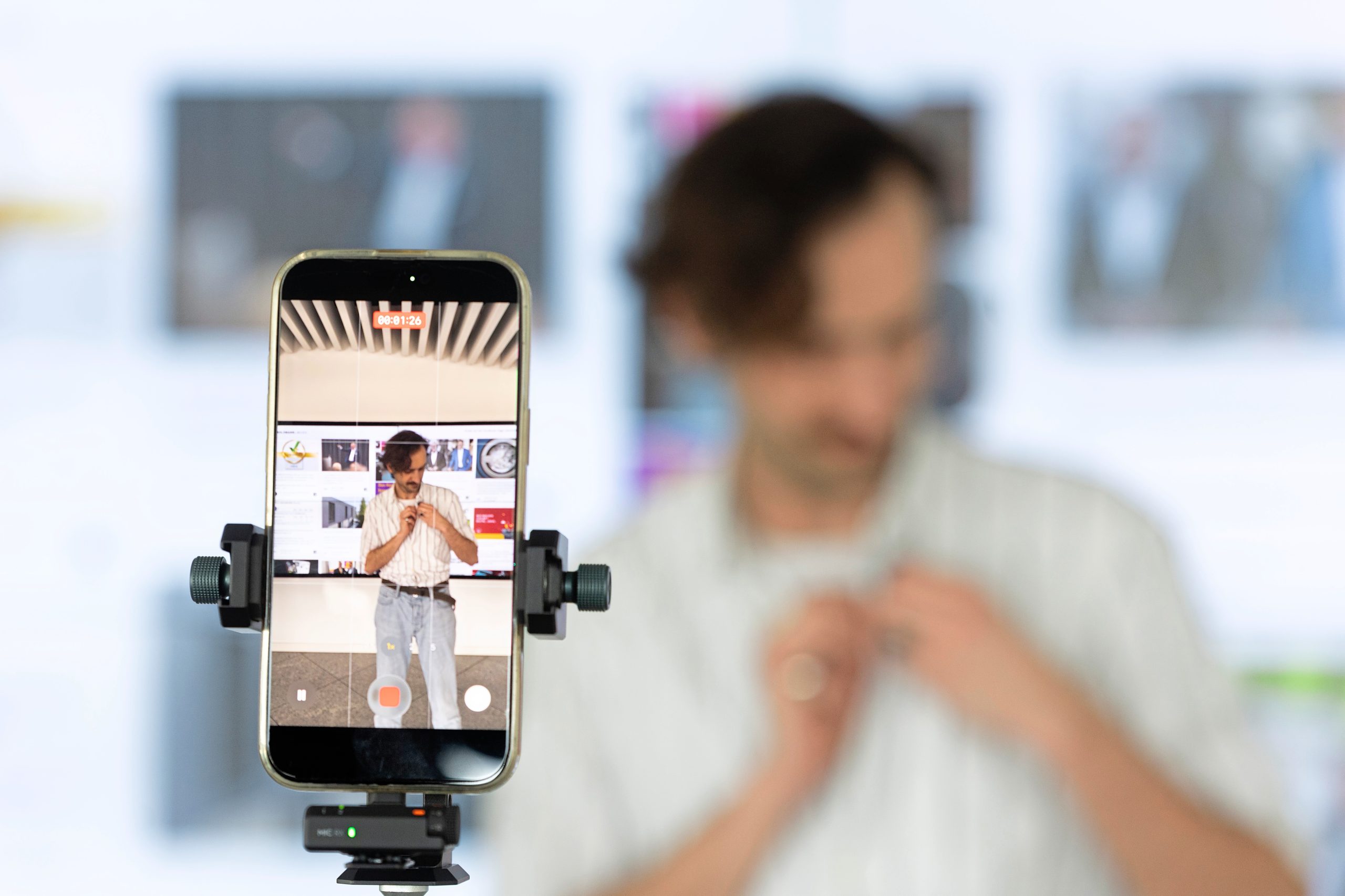Im Vordergrund steht ein Smartphone auf einem Stativ, im Hintergrund steht unscharf zu sehen ein Volontär bei der Aufnahme eines Videos für Social Media.